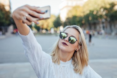 Genç kadın bir selfie cep telefonuyla alıyor. Şehir arka plan.