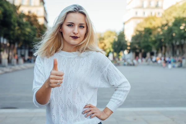 La joven es una maniática y muestra su pulgar hacia arriba. Fondo de la ciudad — Foto de Stock