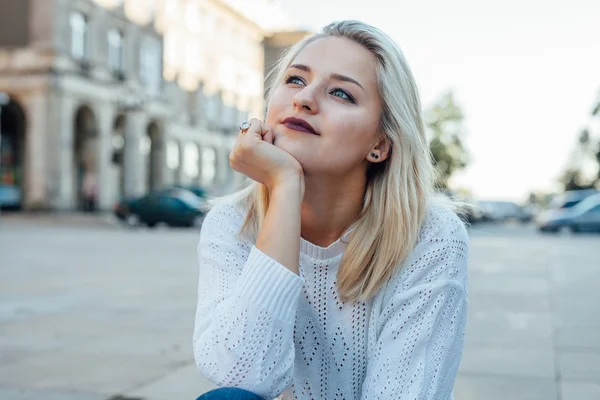 Junge Frau denkt nach und lächelt. Hintergrund der Stadt. — Stockfoto