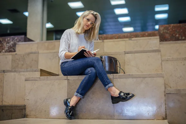 Une jeune étudiante est assise dans les escaliers et écrit quelque chose — Photo