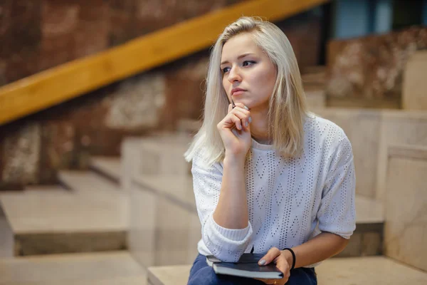 Kvinnlig student sitter på trappan medan du håller notebook och t — Stockfoto