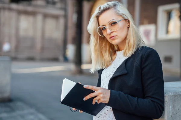 Młoda kobieta jest patrząc na kamery i gospodarstwa notepa — Zdjęcie stockowe