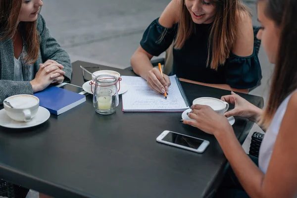 Tres mujeres jóvenes están aprendiendo y hablando en el café al aire libre r — Foto de Stock