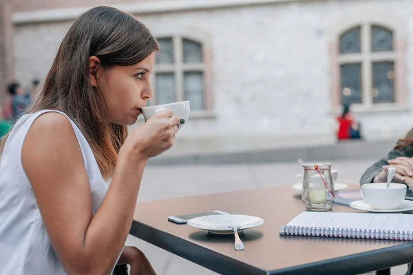 Junge Frau trinkt Kaffee am Tisch. Hintergrund der Stadt. — Stockfoto