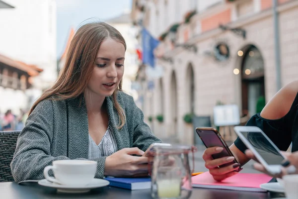 Młoda kobieta jest za pomocą jej telefon komórkowy z jej koleżanki. O — Zdjęcie stockowe