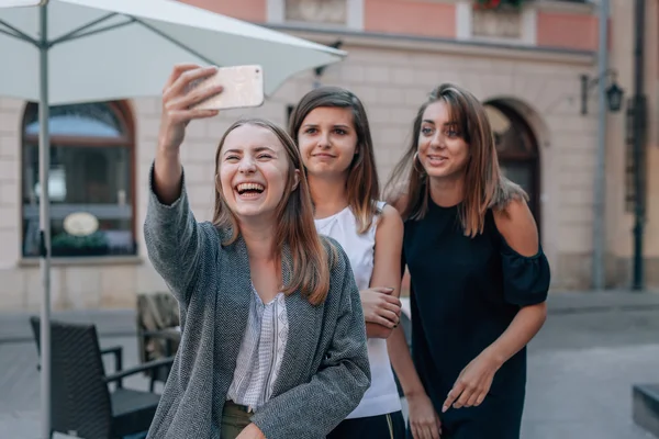 Trzy dziewczyny są biorąc selfie przy użyciu telefonu komórkowego. Miasto zadumany — Zdjęcie stockowe