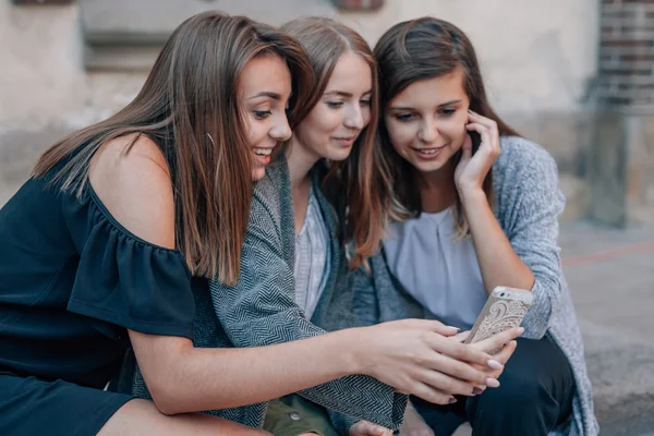 Tres chicas están sentadas en las escaleras de las calles y usando un teléfono inteligente . — Foto de Stock