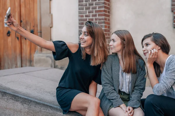 Três meninas estão sentadas nas ruas escadas e tomando usin selfie — Fotografia de Stock