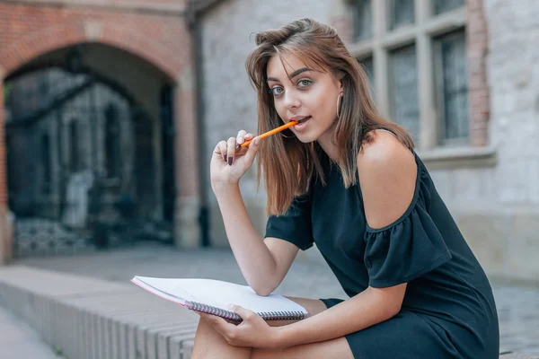 Giovane studente è seduto e tenendo la penna in bocca. Città indietro — Foto Stock