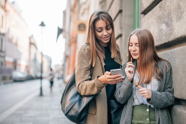 Dvě mladé dívky jsou procházky a pomocí mobilního telefonu. Ulice backg — Stock fotografie