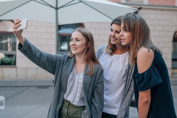 Tre flickor tar selfie med mobiltelefon. Staden bak Royaltyfria Stockbilder