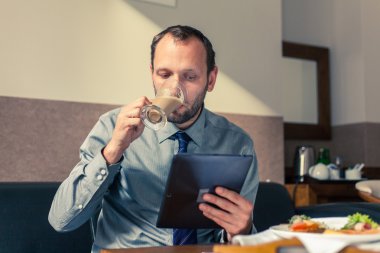 Kahvaltı sırasında tablet üzerinde çalışan iş adamı