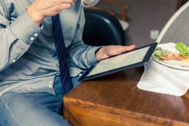 Kahvaltı sırasında tablet üzerinde çalışan iş adamı