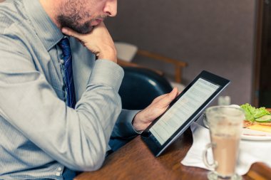 Kahvaltı sırasında tablet üzerinde çalışan iş adamı