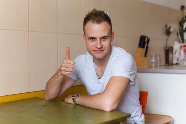 Mann sitzt in Küche und zeigt Daumen hoch. — Stockfoto