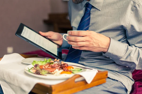 Kahvaltı sırasında tablet üzerinde çalışan iş adamı