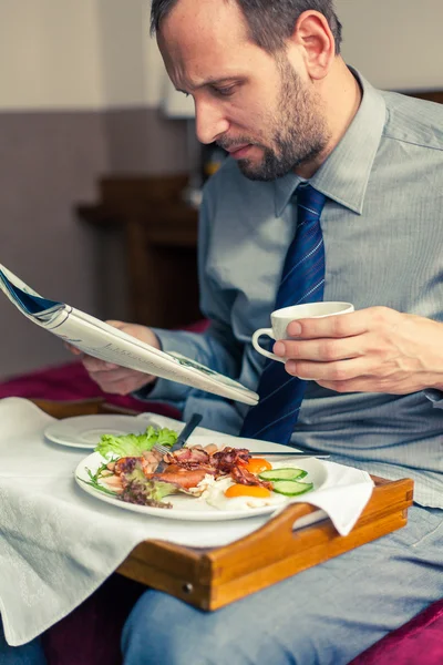 Businessman reading newspaper during breakfast — Stock Photo, Image