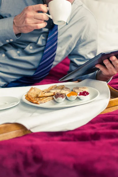 Kahvaltı sırasında tablet üzerinde çalışan iş adamı — Stok fotoğraf