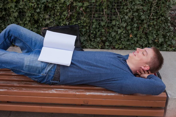 Estudiante descansa con libro en banco de madera — Foto de Stock