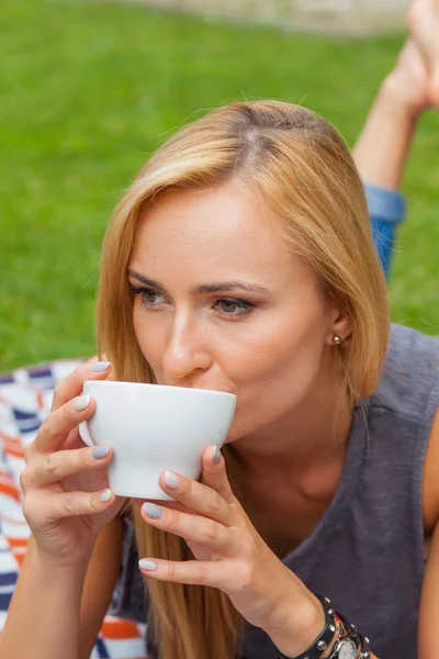 Frau liegt im Park und trinkt Kaffee — Stockfoto