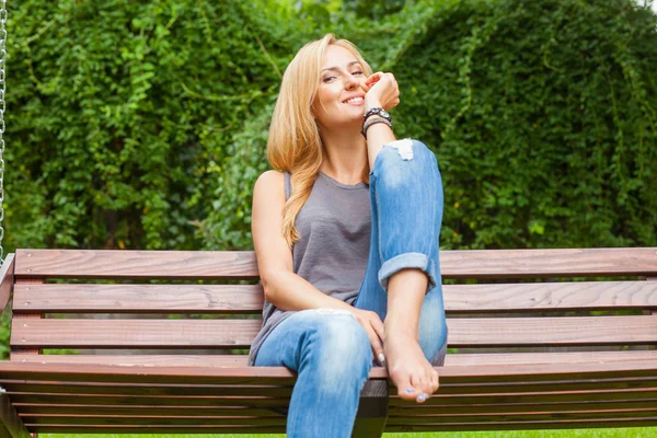 Žena sedí v parku na dřevěné lavici — Stock fotografie