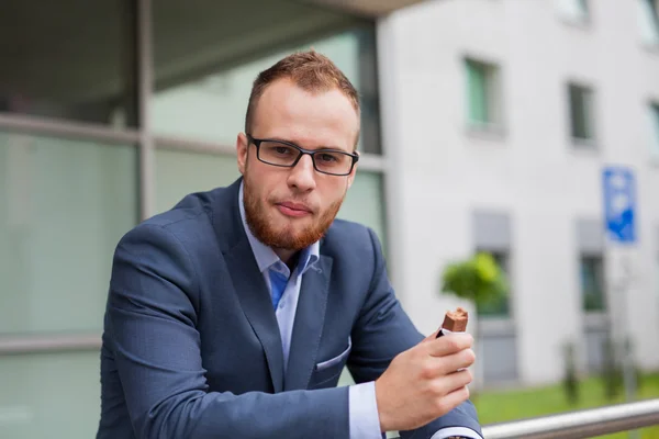 Businessman with beard eating candy bar — Stock Photo, Image