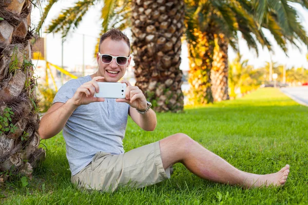 Toeristische onder palm met mobiele telefoon — Stockfoto