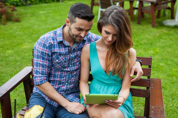 Para siedzi na ławce i za pomocą tabletu — Zdjęcie stockowe