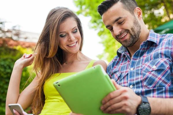 Par sitta på bänken och använder tablet — Stockfoto