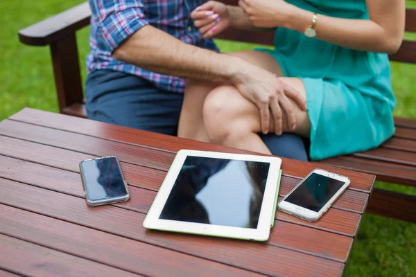 Tableta, smartphones cerca de pareja sentada . — Foto de Stock