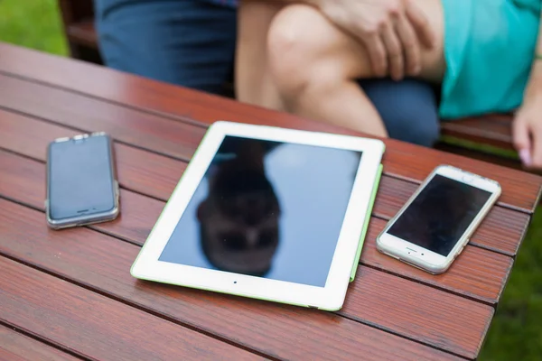 Tableta, smartphones cerca de pareja sentada . —  Fotos de Stock