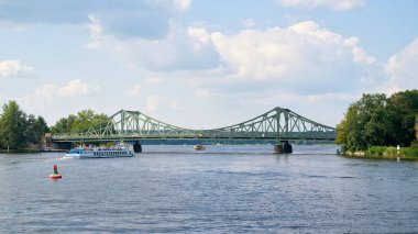 Berlin, Almanya - 17 Temmuz 2021: Potsdam ve Berlin arasındaki Havel Nehri üzerindeki Glienicke Köprüsü. Ön planda turistlerle dolu bir gezi teknesi var..                                