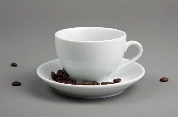 Кофейные зерна, вытекающие из чашки кофе на сером фоне . — стоковое фото