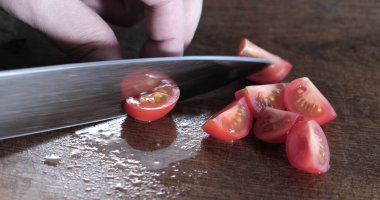 Ahşap kesme tahtasıyla domatesleri bıçakla kesen şef.