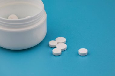 Mavi arka plandaki ilaç kutusundan beyaz haplar dökülüyor.