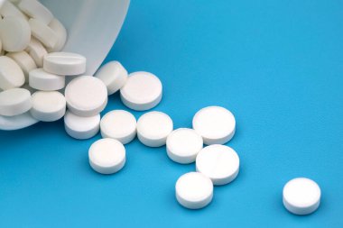 Mavi arka plandaki ilaç kutusundan beyaz haplar dökülüyor.