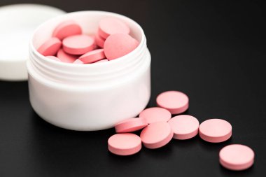 Siyah arka plandaki ilaç kutusundan pembe haplar dökülüyor.