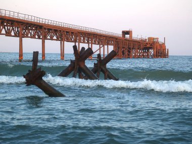 Eski bir demir paslı iskele, rıhtım, mavi denizde bir köprü turuncu renge boyanmış sabah güneşinin ışınlarıyla.