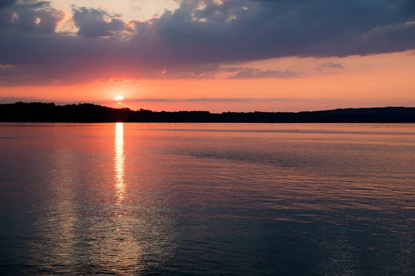 沈む太陽や灰色やピンク色の雲からの反射で湖に沈む夕日 — ストック写真