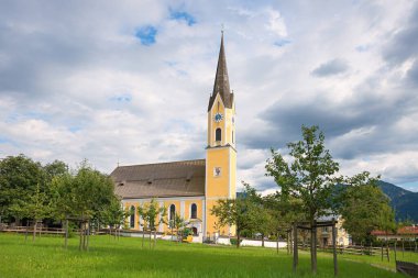 St. Sixtus Katolik Kilisesi, Schliersee turizm beldesi, bulutlu bir arka plan. Elma ağaçlı yeşil çayır.
