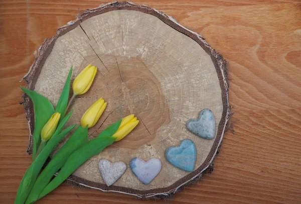 Fondo rústico de madera con rebanada de árbol, tulipanes y corazón de piedra — Foto de Stock