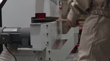 İşçi, sanayi makinesinin kenarından ahşap parça alıyor. Ahşap işleme, modern ekipman ve üretim sürecine yakın çekim