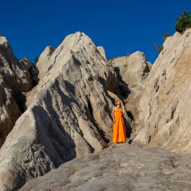 Kanyonun kıyısındaki kumlu dağlar arasında turuncu elbiseli bir kız.