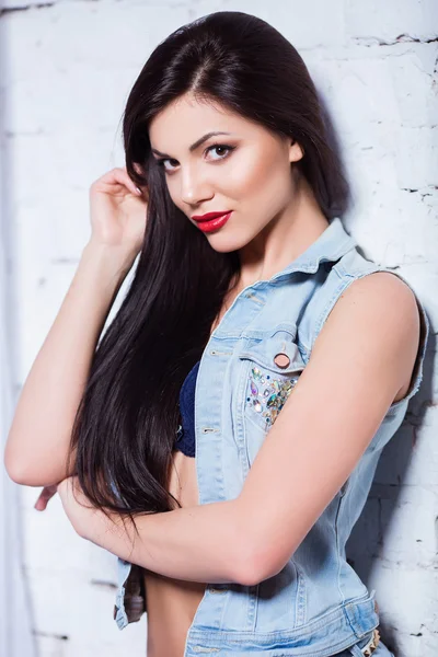 Jovem atraente bela mulher morena olhando para a câmera. Menina sexy com cabelo preto longo posando em jeans . — Fotografia de Stock