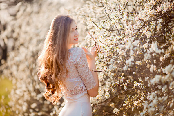 Happy beautiful young woman relaxing in blossom park. Attractive female in white dress enjoy fresh flowers. Toned image