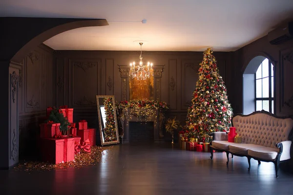 Interior of luxury dark living room with fireplace, comfortable sofa and chandelier decorated with Christmas tree and gifts