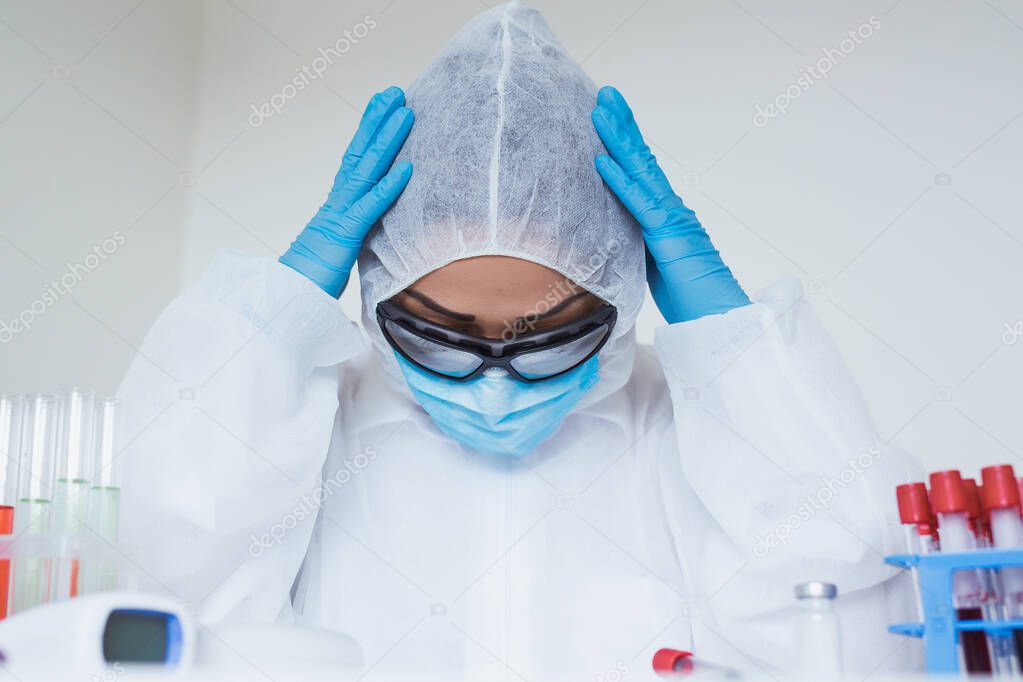 Stressed female doctor sitting tired at his desk. Mid adult female doctor working long hours in protective clothes. Covid-19 overworked doctor in his office needs a break.