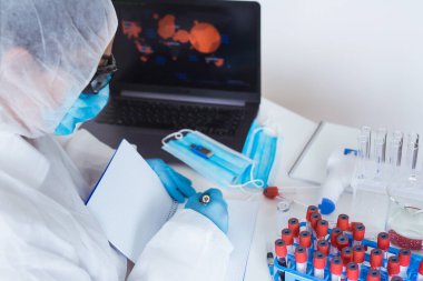 Koruyucu maske, kan örneği tüpleri ve laboratuvar teknisyenlerinin elleri arka planda. Coronavirus COVID-19 Laboratuar Analizi İş Yeri.