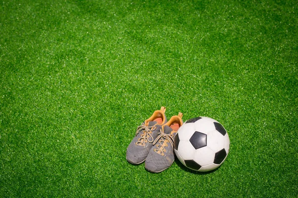 Futebol, bola de futebol e sapatos esportivos na grama verde — Fotografia de Stock