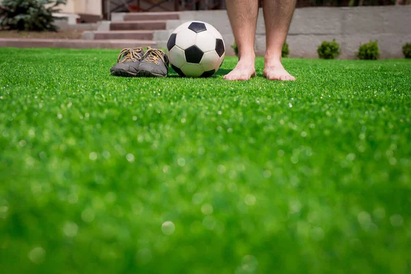 Ноги неузнаваемого босоногого футболиста против искусственной травы. Футбольный мяч, обувь для уличного футбола. Копирование пространства. — стоковое фото